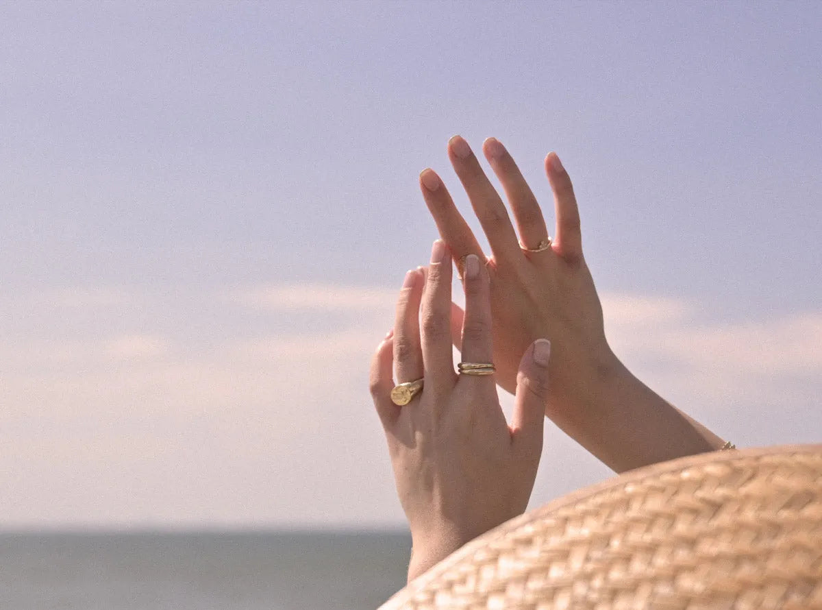 hands wearing summer jewellery on a beach infront of a blue sky