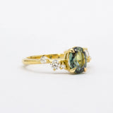 Gold ring with a greeny blue gemstone and smaller diamonds on a white background