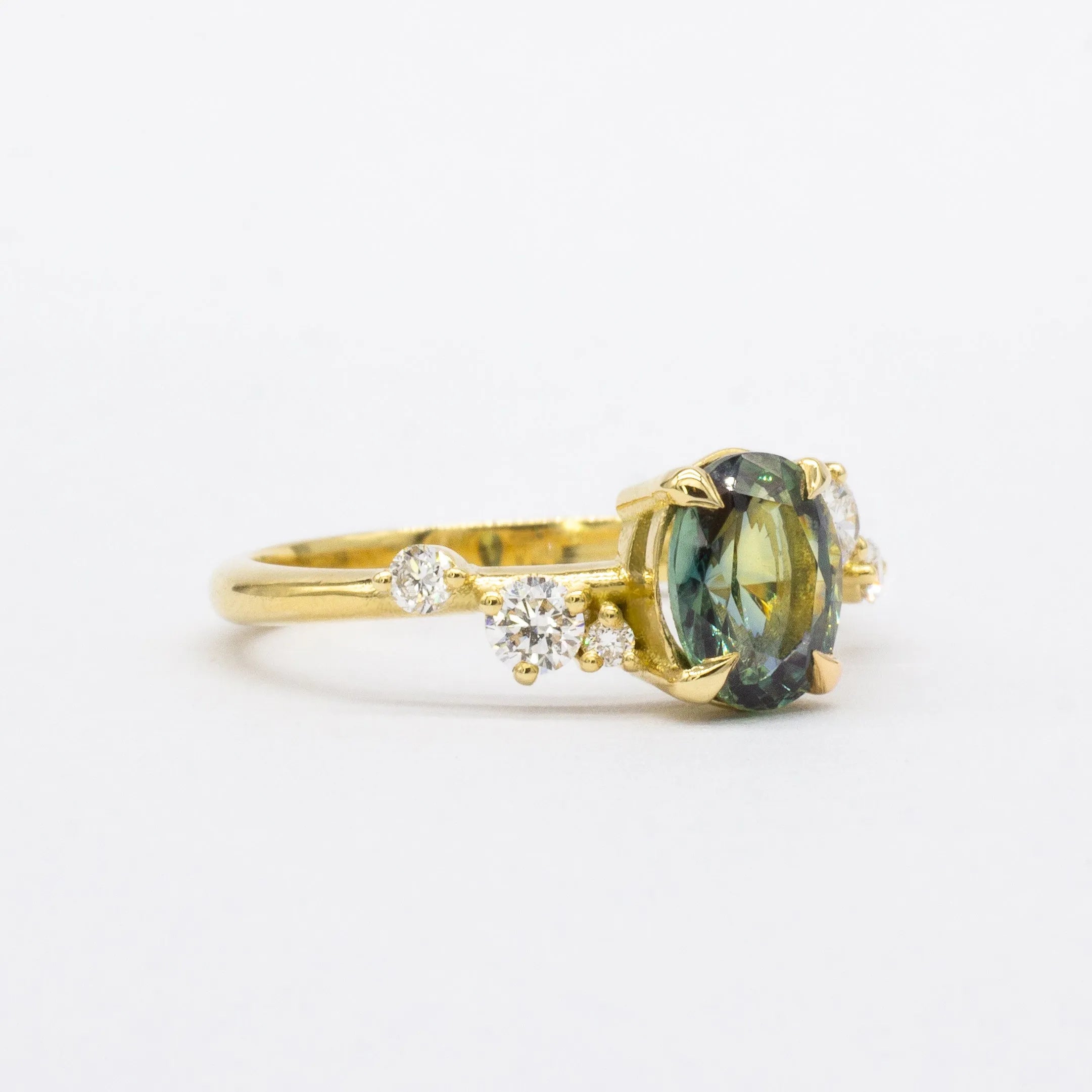 Gold ring with a greeny blue gemstone and smaller diamonds on a white background