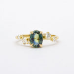 Gold ring with a green gemstone and diamond accents on a white background