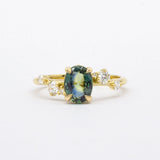 Gold ring with a green gemstone and diamond accents on a white background