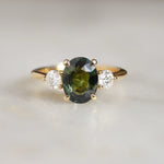 engagement ring with large green sapphire and smaller diamonds on marble surface