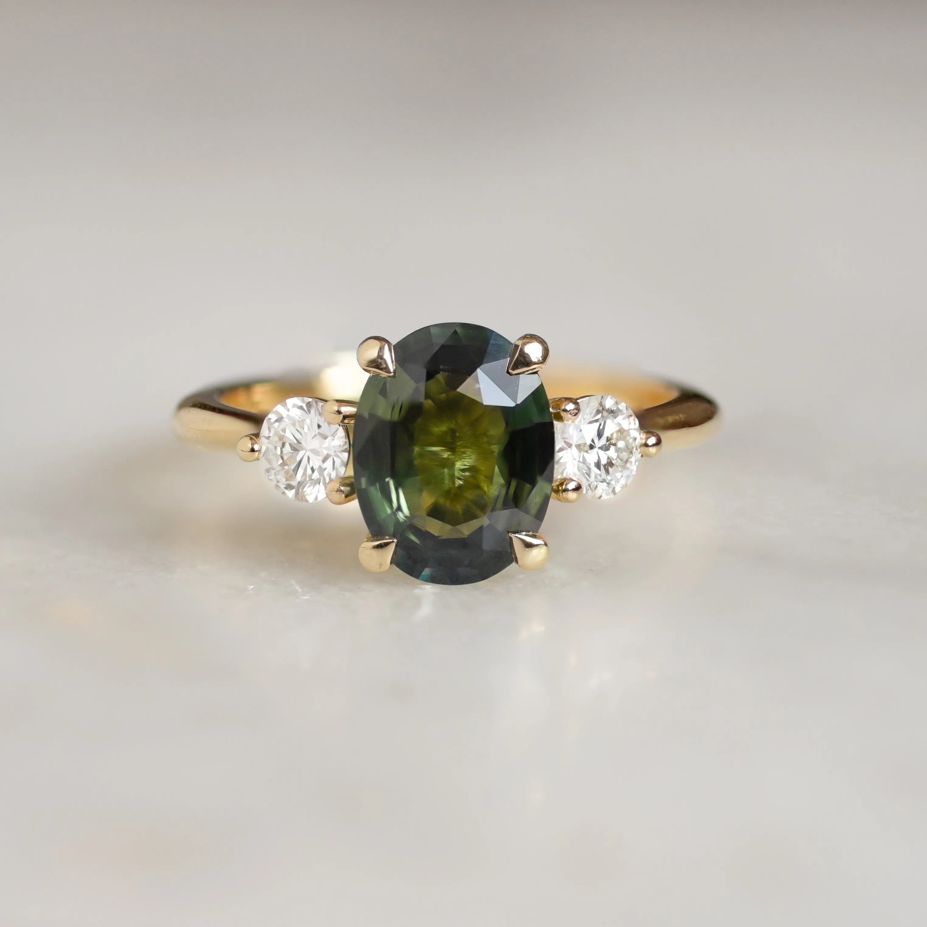 engagement ring with large green sapphire and smaller diamonds on marble surface