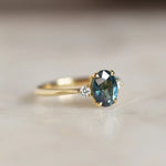 gold ring with large teal sapphire and small round diamonds on marble surface