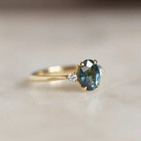 gold ring with large teal sapphire and small round diamonds on marble surface