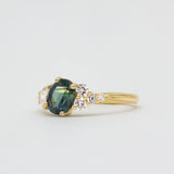 Gold ring with a blue green sapphire and diamonds on a light gray background