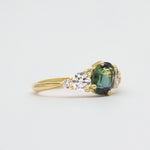 Side view of asymmetric engagement ring with a green blue gemstone and diamond on a light gray background