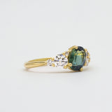 Side view of asymmetric engagement ring with a green blue gemstone and diamond on a light gray background