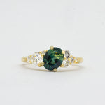 Gold ring with a green blue gemstone and diamond accents on a light gray background