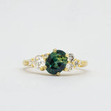 Gold ring with a green blue gemstone and diamond accents on a light gray background