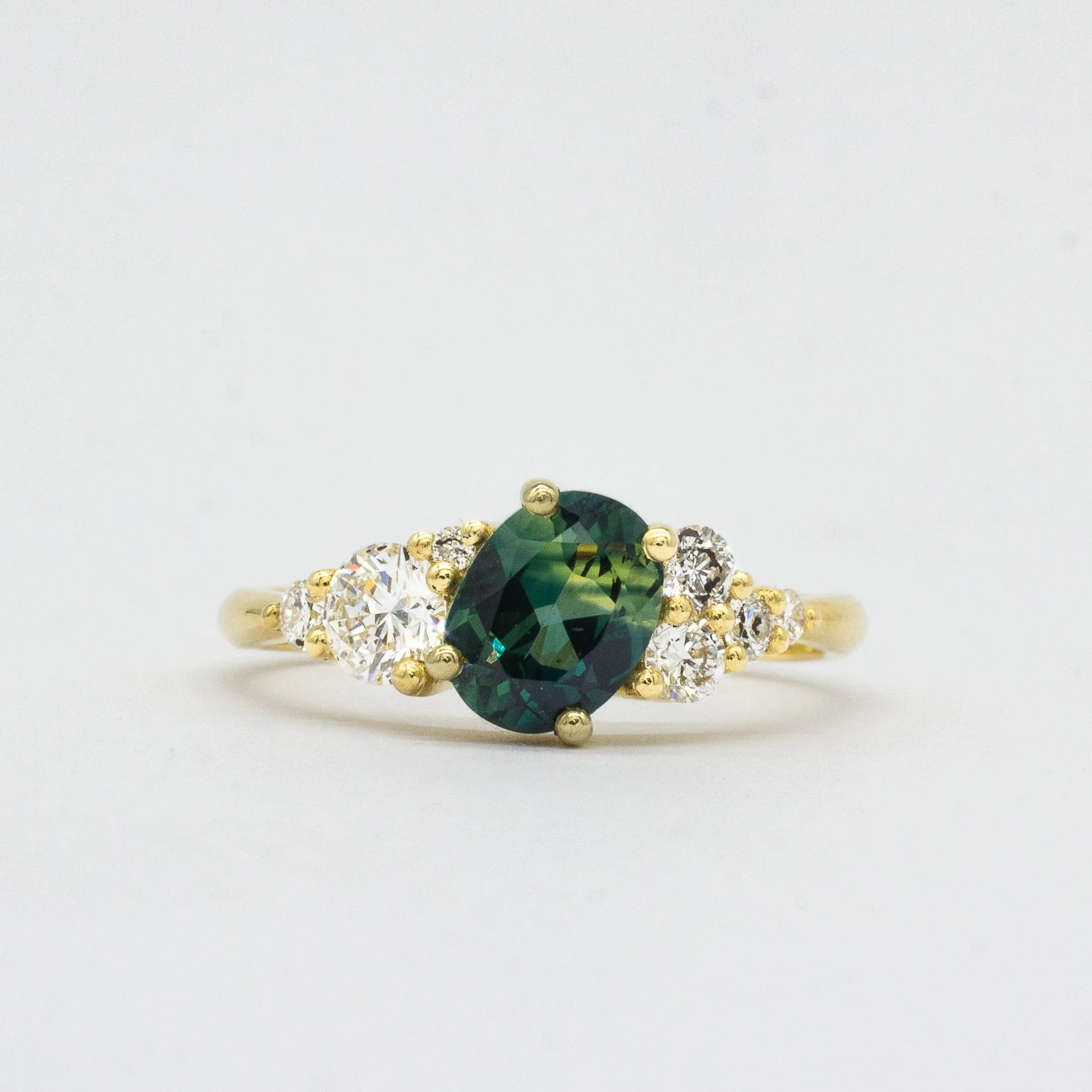 Gold ring with a green blue gemstone and diamond accents on a light gray background