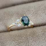 blue green oval sapphire engagement ring with cluster of round diamonds in ring box slot