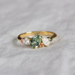 asymmetrical green and pink sapphire engagement ring with diamonds on neutral fabric