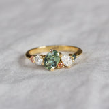 asymmetrical green and pink sapphire engagement ring with diamonds on neutral fabric