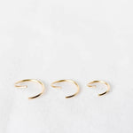 Three open gold cartilage hoop earrings on a white background