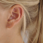 Close-up of an ear wearing two gold hoop earrings with blonde hair.