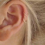 Close-up of an ear wearing gold hoop earrings with blonde hair.