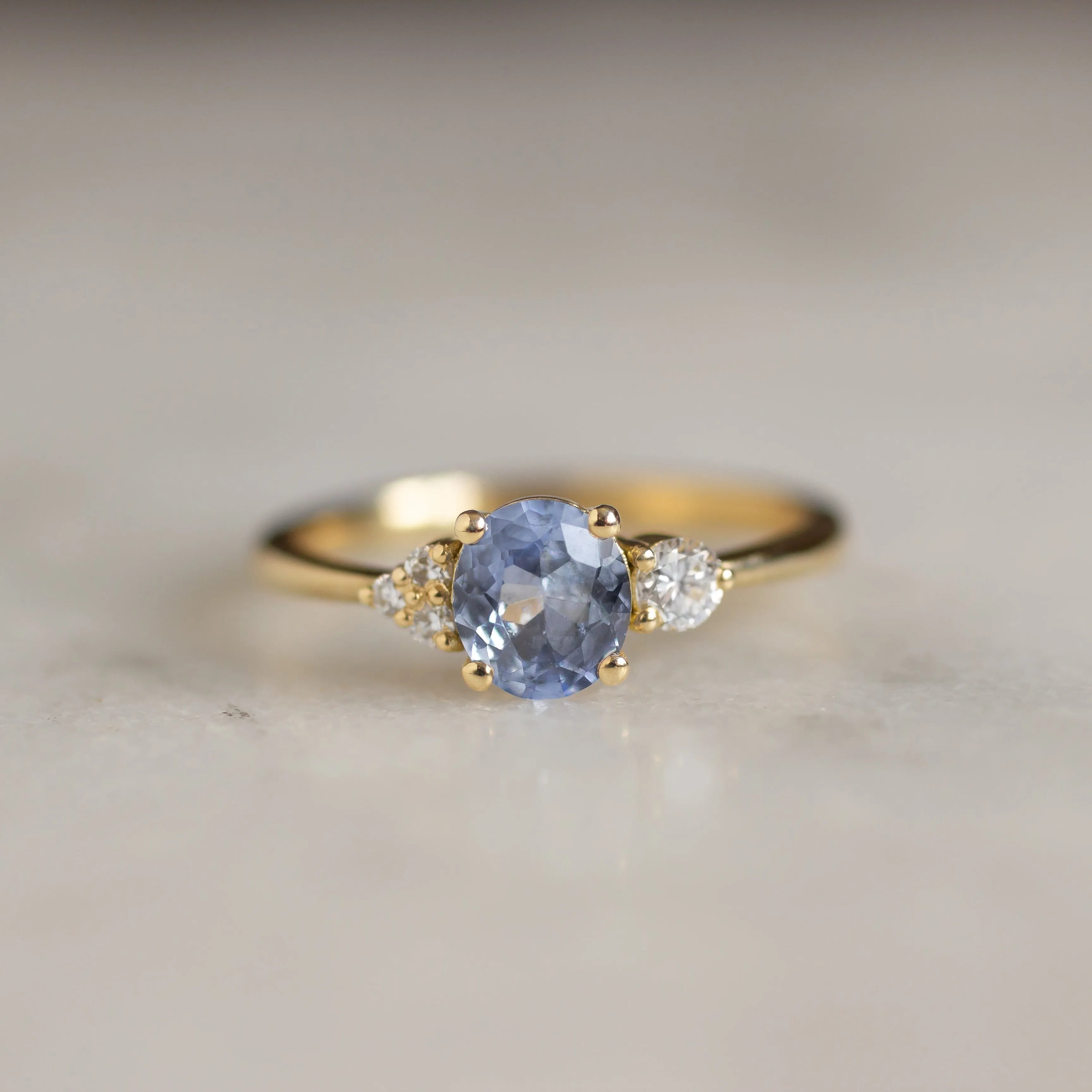 close up of light blue sapphire engagement ring on marble surface
