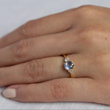 close up of hand wearing cornflower blue sapphire engagement ring with asymmetric diamond cluster