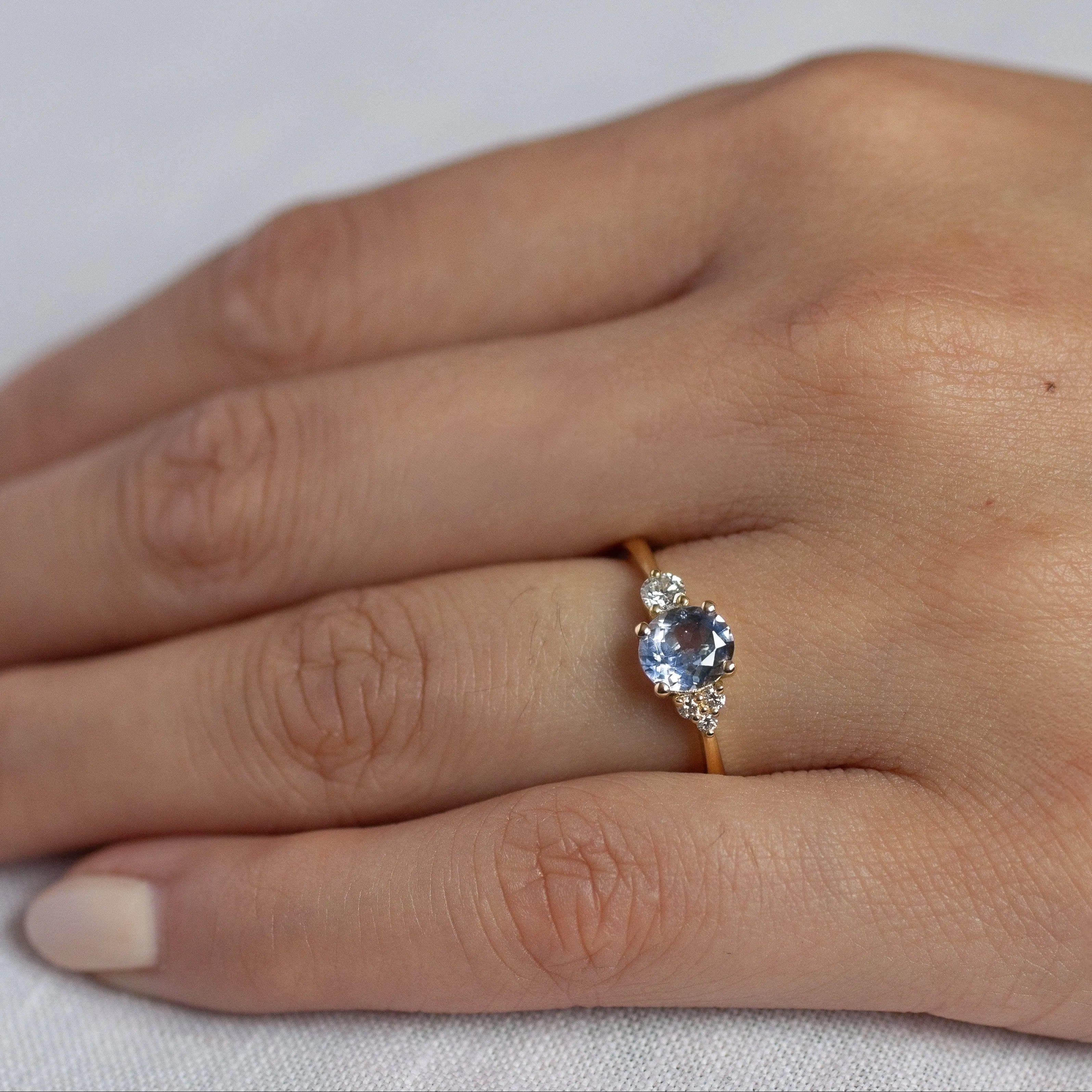 close up of hand wearing cornflower blue sapphire engagement ring with asymmetric diamond cluster