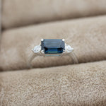 close up of white gold engagement ring with blue sapphire, round diamonds in ring box slot