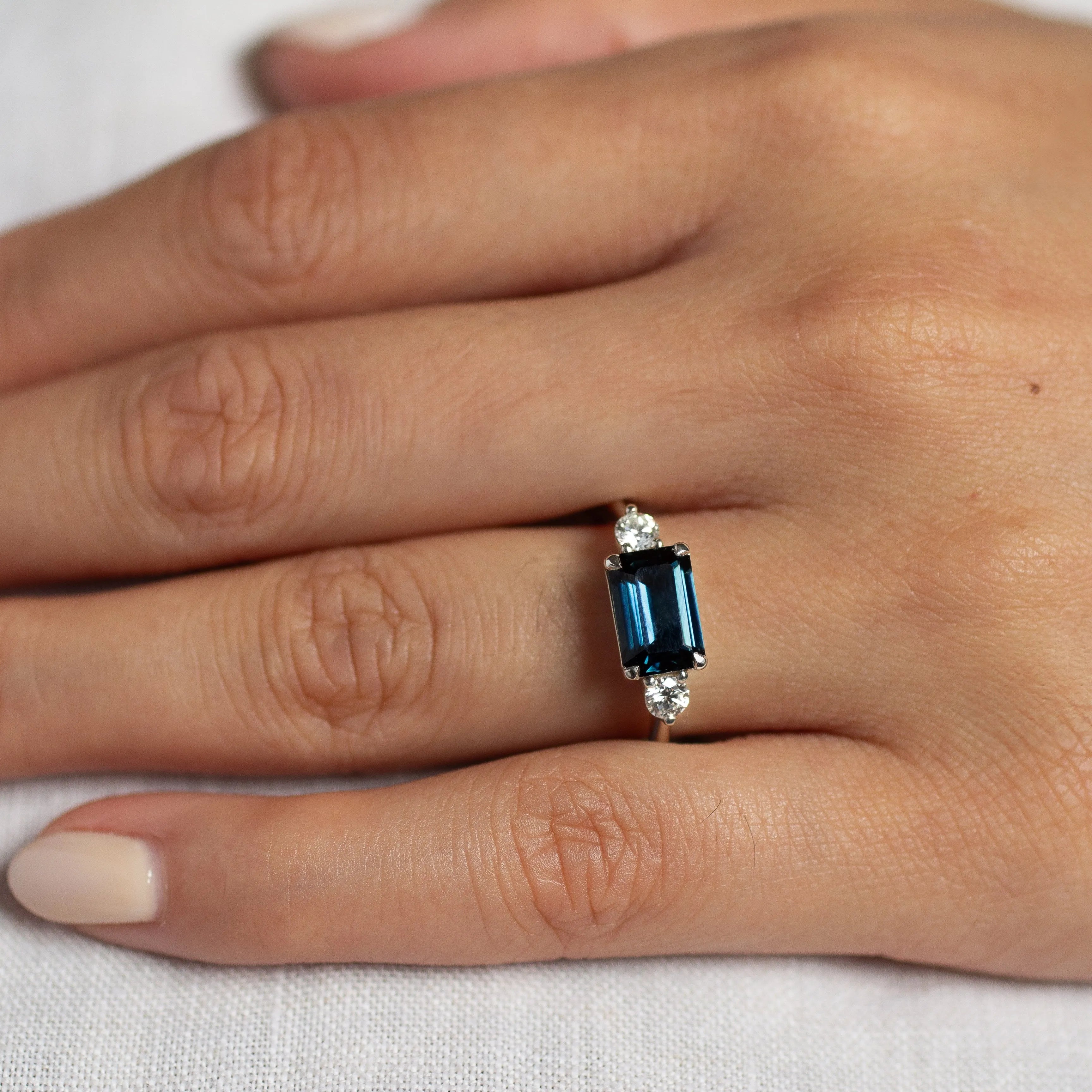 close up of hand wearing engagement ring with dark blue emerald cut sapphire and round diamonds