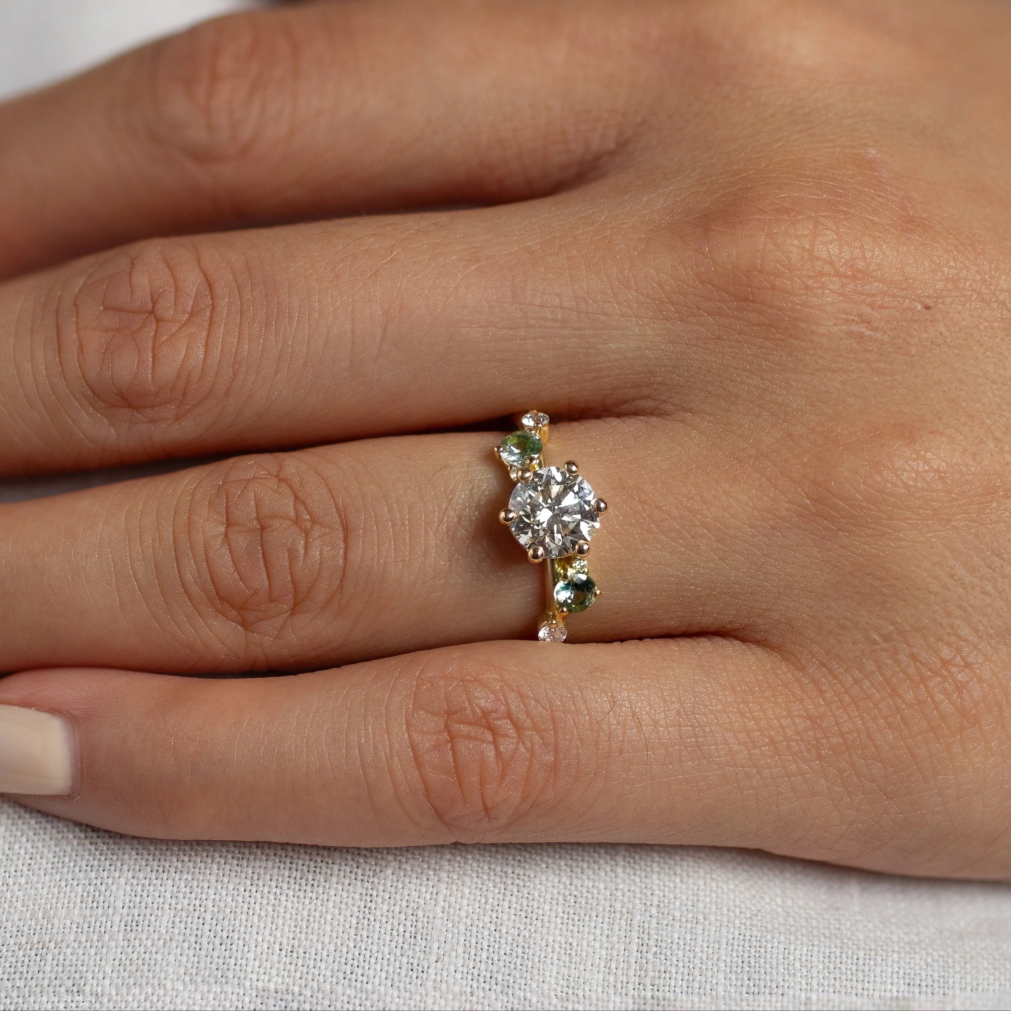 Hand wearing a diamond ring with round diamond and small round sapphires on a light background