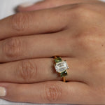 Hand wearing a ring with a diamond and green gemstones on a white background