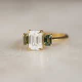 engagement ring with rectangle diamond and green sapphires with gold band and claws with blur background