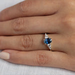 close up of hand wearing 5 stone white gold engagement ring with blue oval sapphire and diamonds