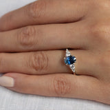 close up of hand wearing 5 stone white gold engagement ring with blue oval sapphire and diamonds