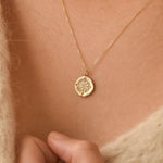 Gold compass necklace with a round pendant on a person's neck