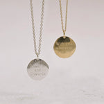 Two compass necklaces with engraved text on circular pendants against a light background