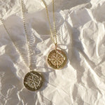 Two gold compass necklaces with compass pendants on a textured white surface