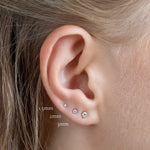 close up of ear wearing 1.5mm, 2mm and 3mm white gold diamond stud earrings with labels