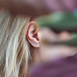 ear wearing three diamond stud earrings with maroon and green leaves blurred in the foreground