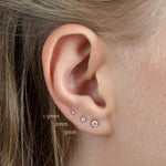 close up of ear wearing 1.5mm, 2mm and 3mm diamond stud earrings in three lobe piercing with labels
