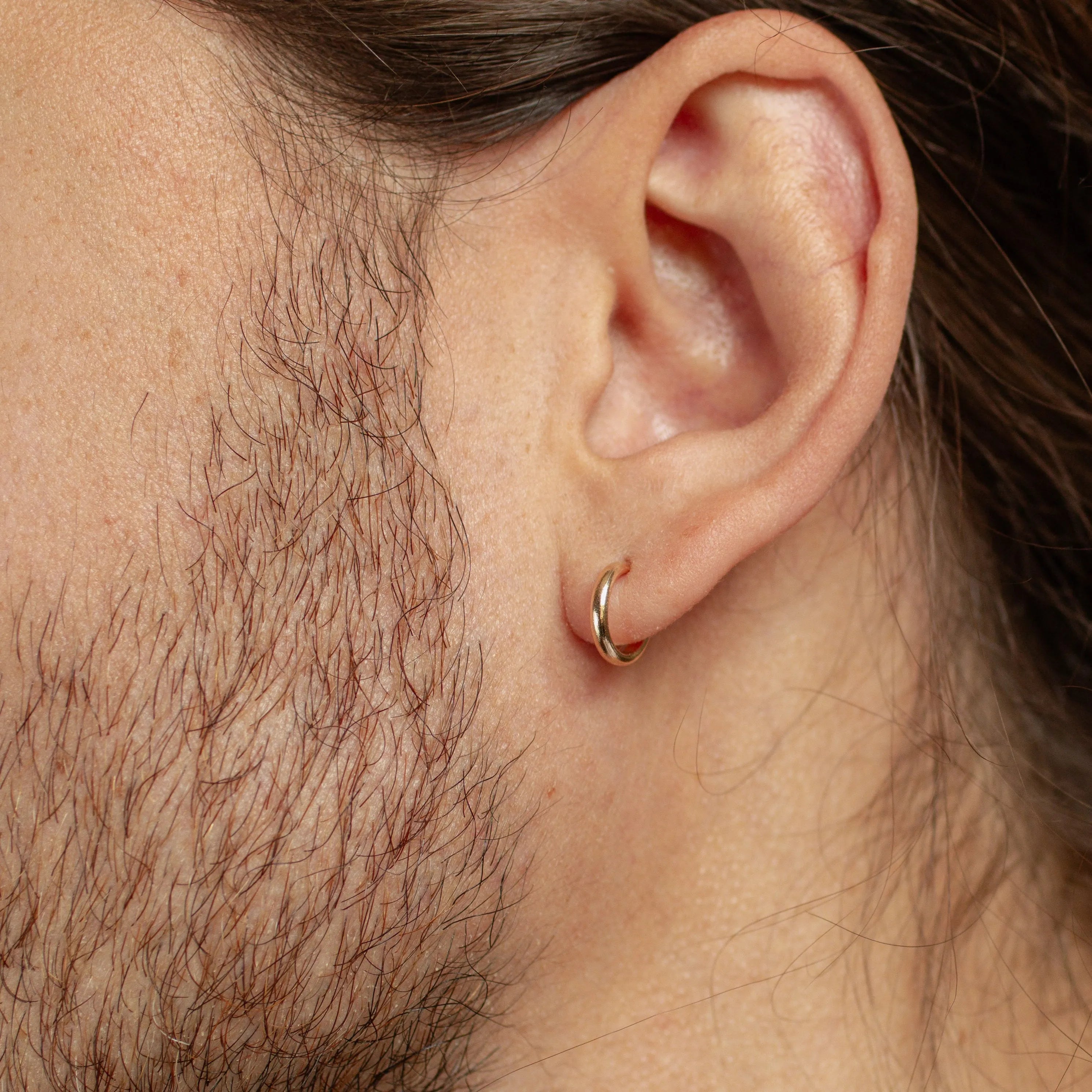 close up of mens ear wearing solid gold huggie hoop earrings