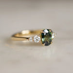 5 stone gold engagement ring with green sapphire on marble surface
