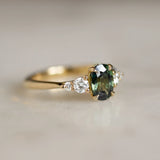 5 stone gold engagement ring with green sapphire on marble surface