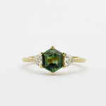 Gold ring with a green hexgaon sapphire and smaller triangular diamonds on a white background