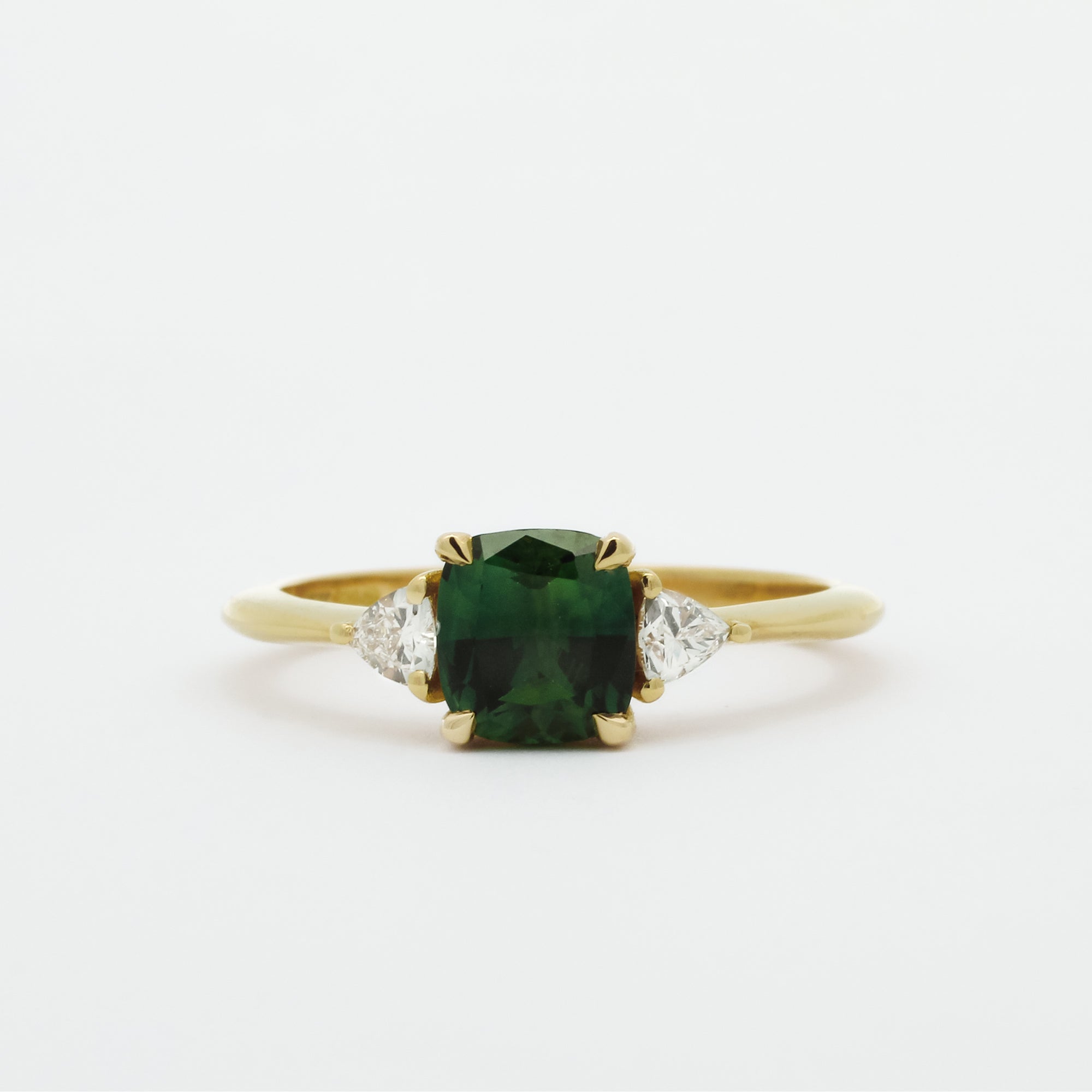 Gold ring with a green cushion cut sapphire and smaller triangle-shaped diamonds on a white background