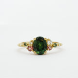 Gold ring with a green gemstone and smaller pink and diamonds on a white background