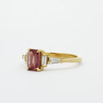 Gold ring with a peachy berry pink gemstone on a white background