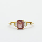 Gold ring with a pink sapphire and baguette diamonds on a white background