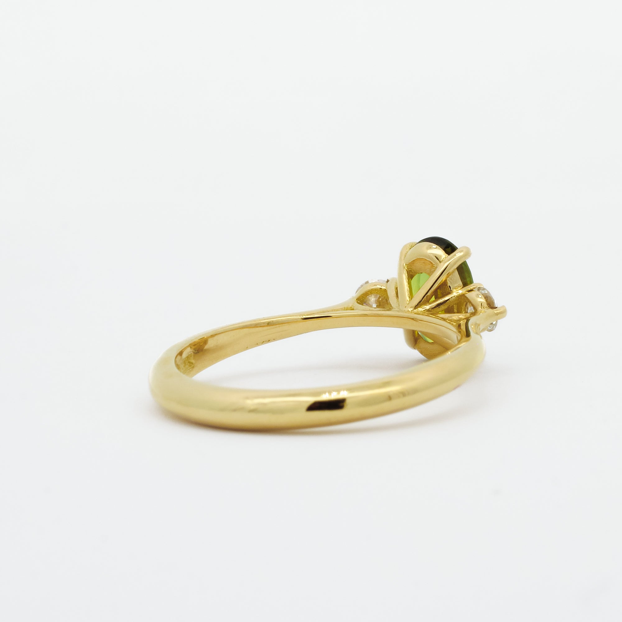 back view of gold engagement ring with a green gemstone on a white background