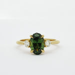 Gold ring with a slim oval sapphire gemstone and smaller diamonds on a white background