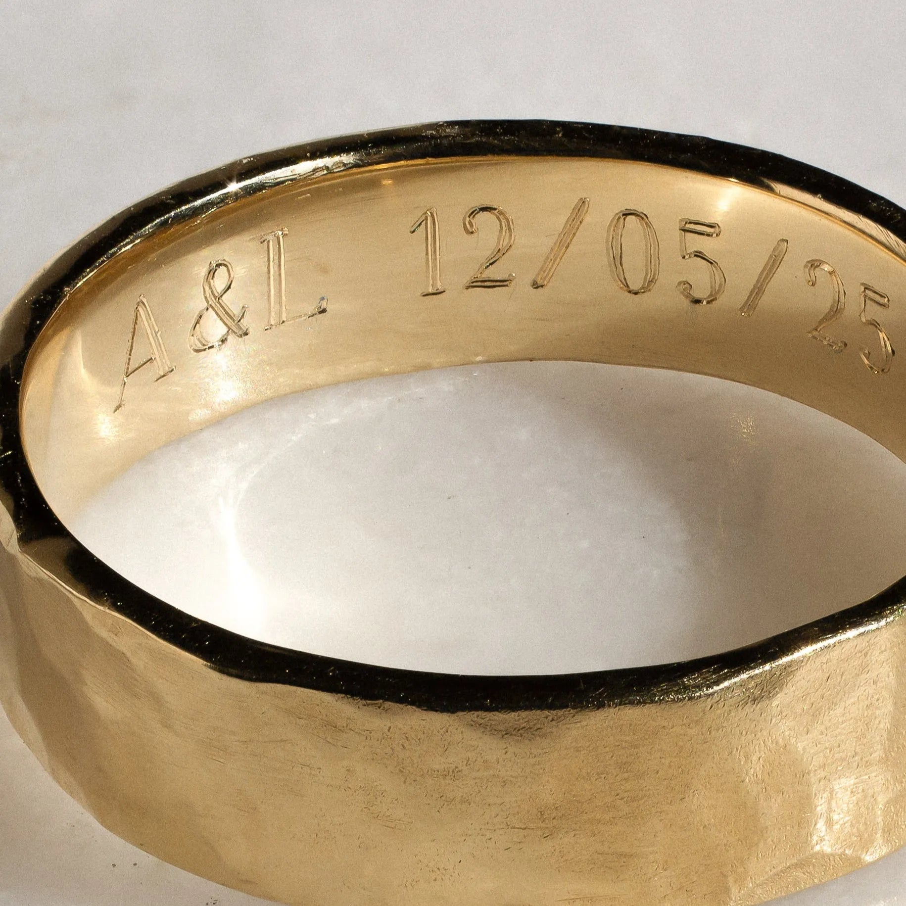 Gold ring with engraved initials and date on a white background