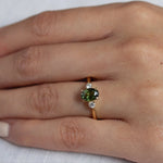 close up of hand wearing forst green sapphire trilogy engagement ring with diamonds and gold band