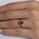 close up of hand wearing forst green sapphire trilogy engagement ring with diamonds and gold band